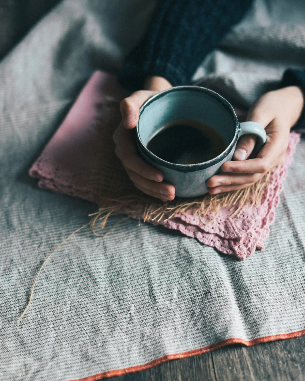 Two hands holding a warm mug of tea on a linen throw