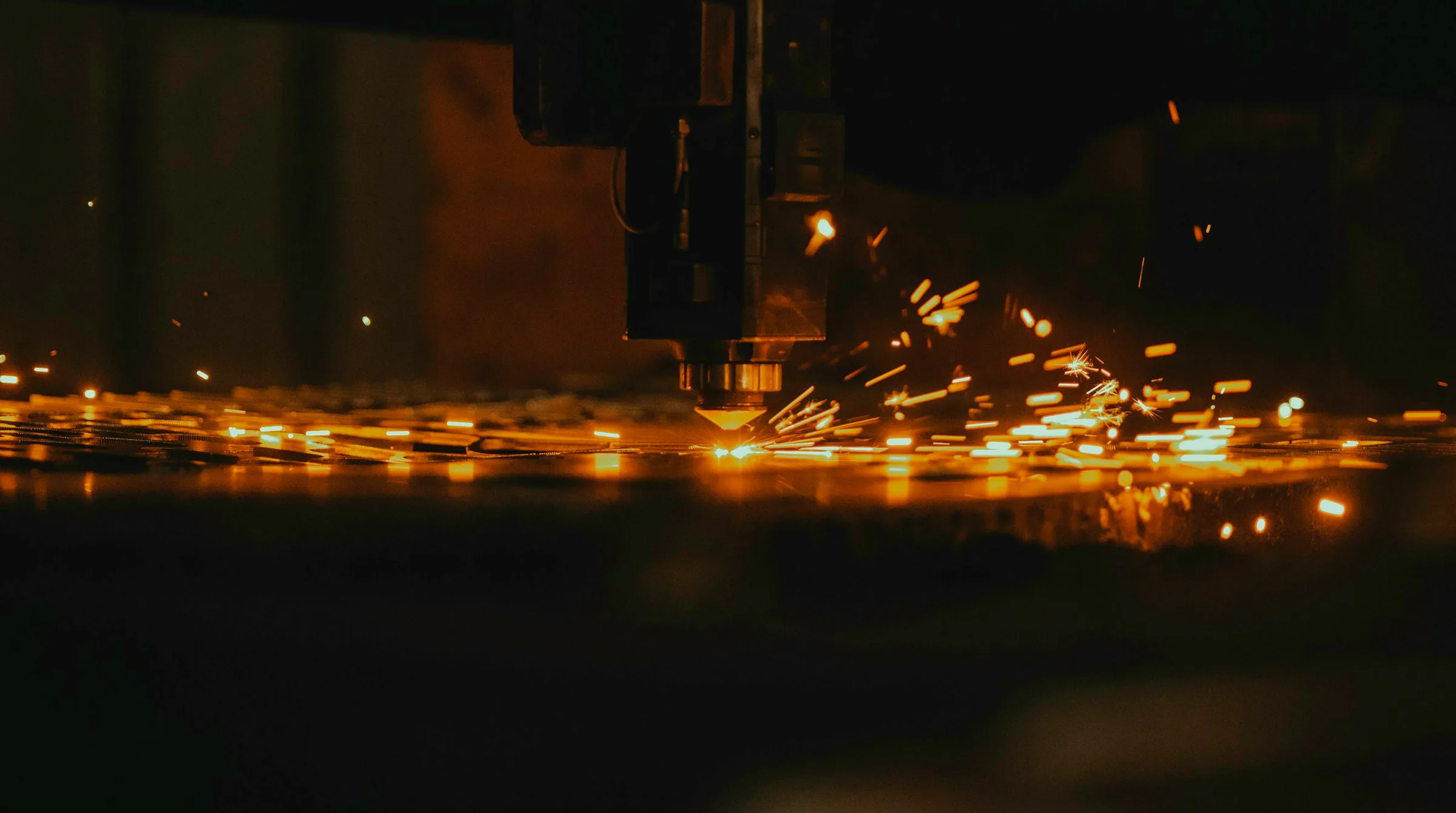 A cutting head throwing sparks across a steel sheet