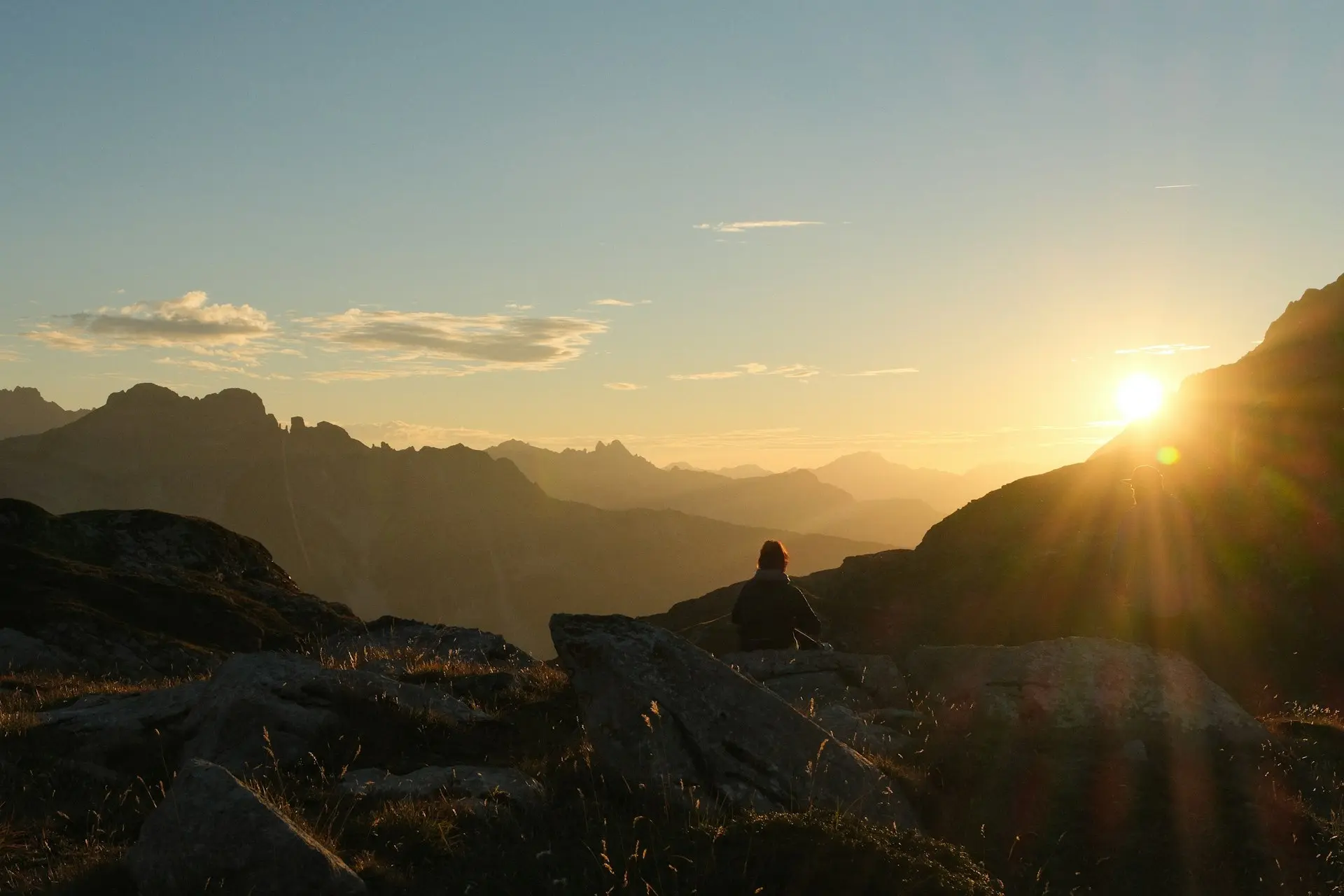 A person sitting on a rocky ridge watching the sun set over the mountains