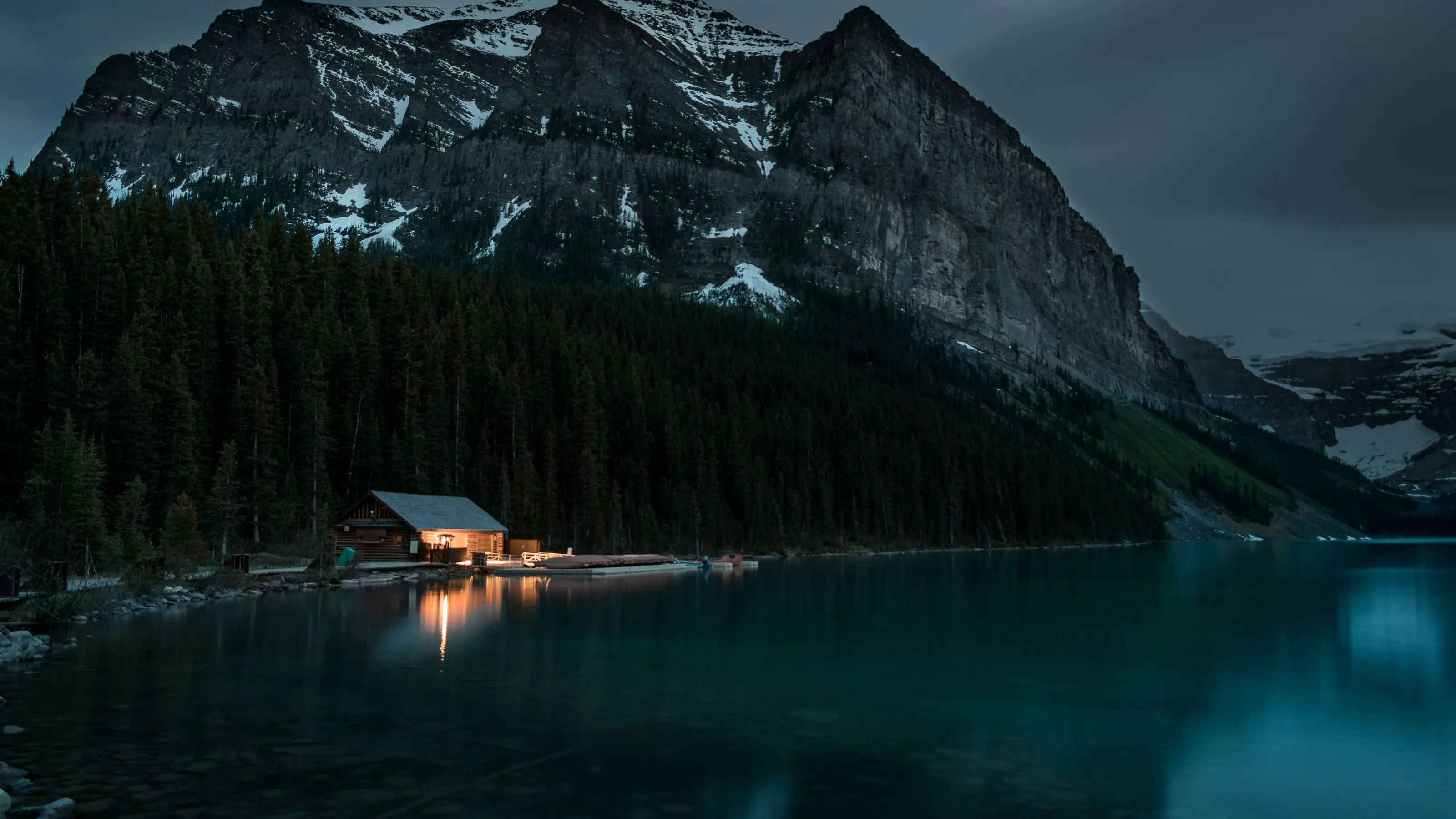 A timber lodge lit up at night on the shore of a still lake