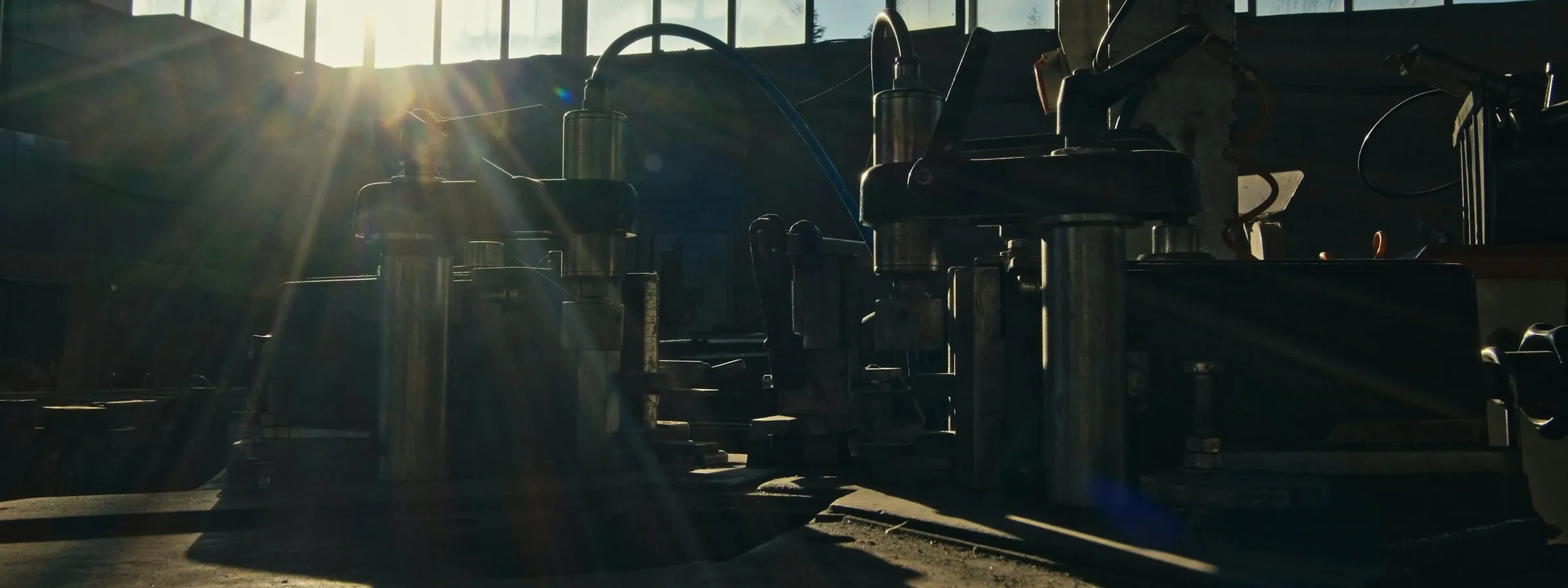 Press heads silhouetted against the sunlit windows of a workshop
